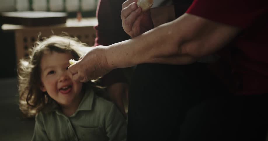 A grandmother gives fruit to her granddaughter to eat