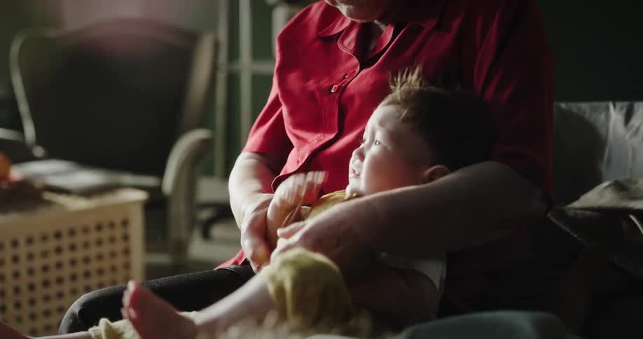 Elderly woman wearing a red shirt holds grandson sitting in armchair