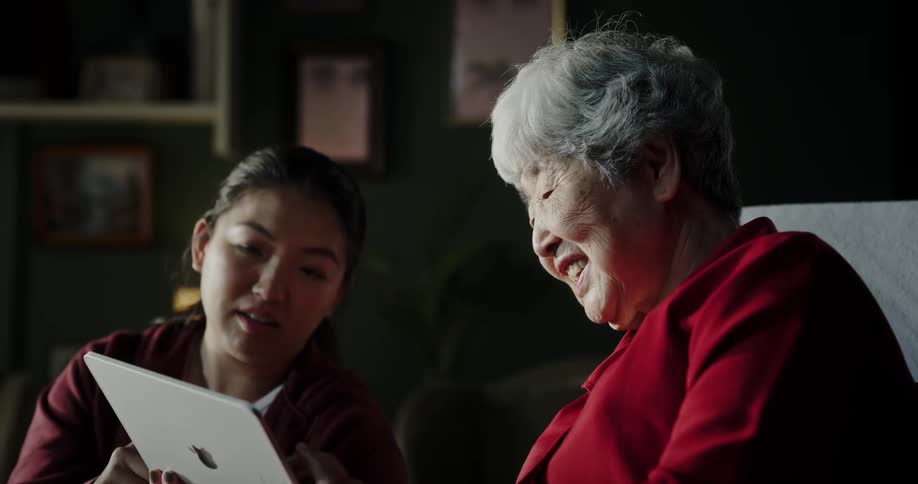 Elderly woman and a woman next to her both swiping their fingers on a tablet
