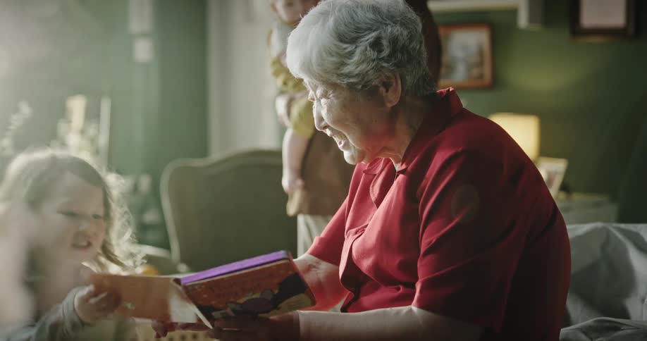 Grandmother sitting holding a book and showing it to her granddaughter