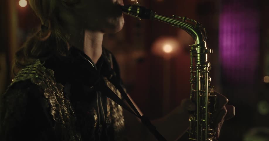 A young woman is standing inside a room practicing her saxophone