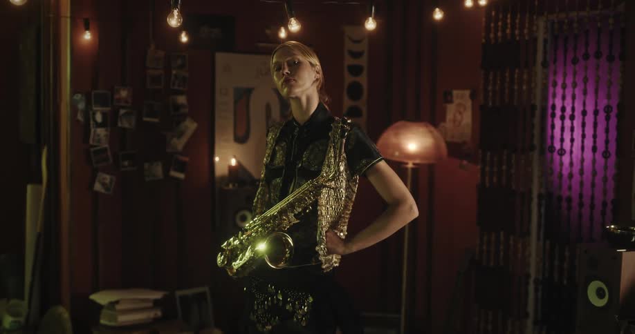 A lady stand still after playing saxophone in a room at night