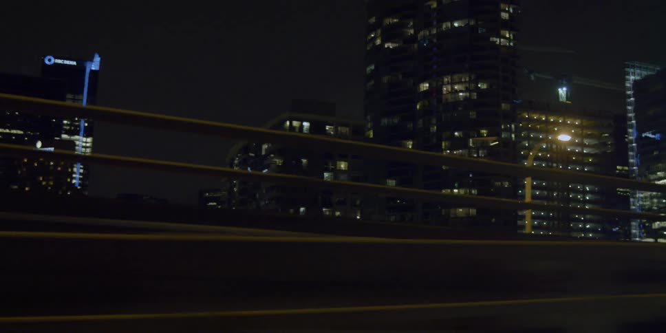 A vehicle drives by city buildings at night