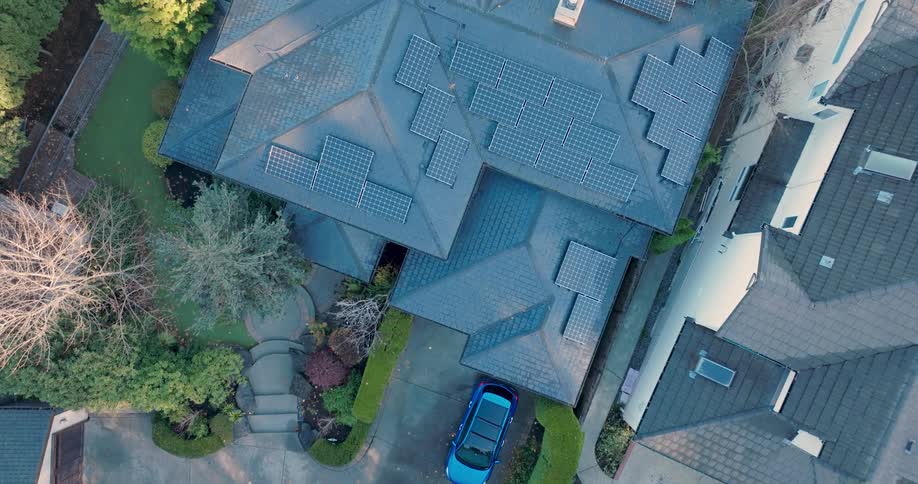 An electric vehicle is in the driveway of a nice home with rooftop solar panels