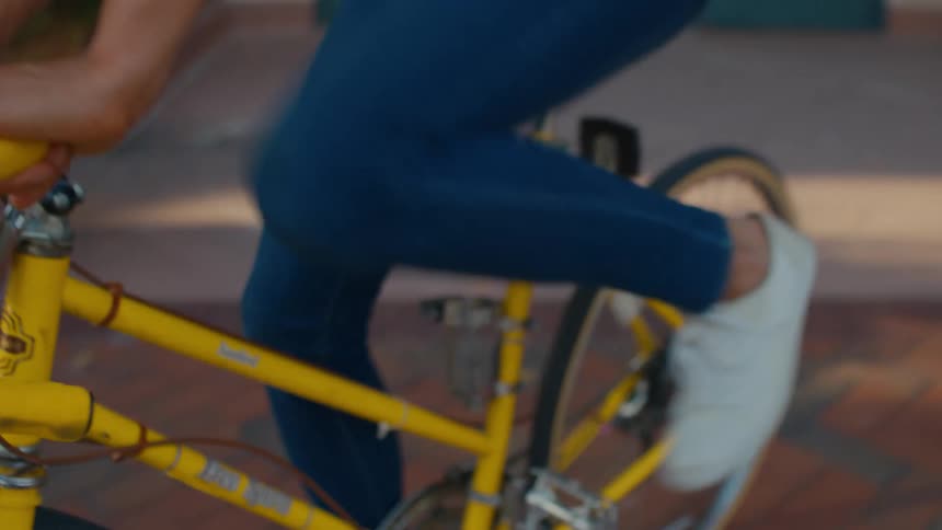 A woman pedals a yellow bicycle during the day