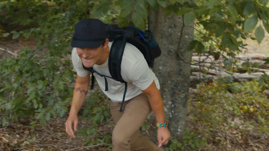 A man wearing a backpack is hiking up a hill in the woods