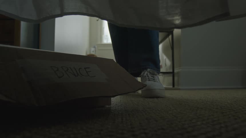 Person walks around bed with labeled cardboard box stored underneath