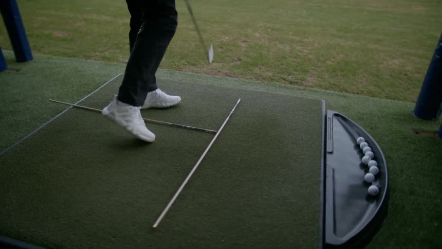 Man wearing white shoes swings a golf club