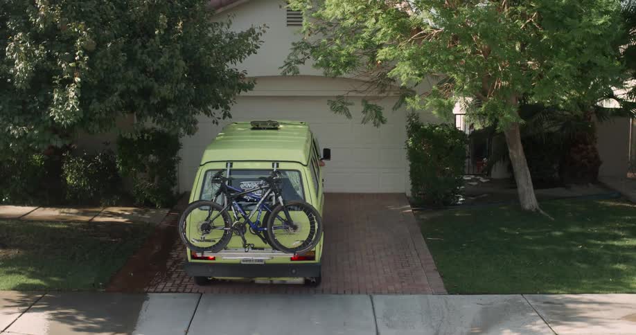 A green van carrying bicycles backs out of a residential driveway