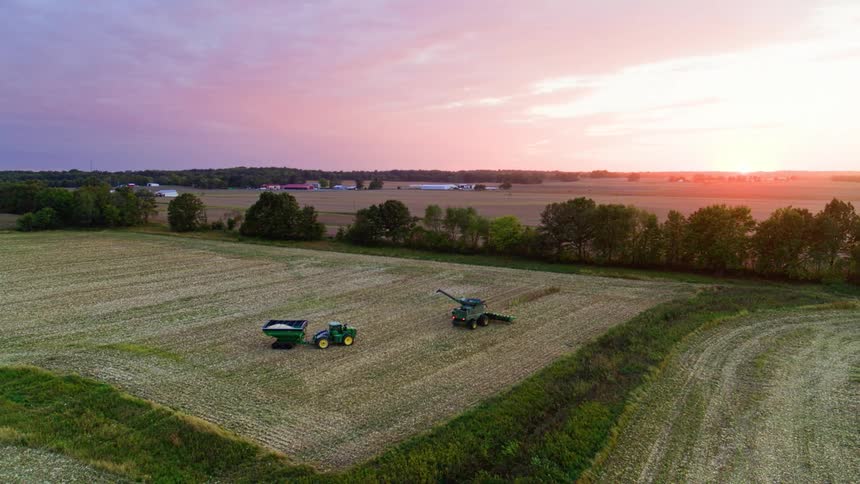 Tractors finish harvesting for the day as dusk sets in the vibrant pink and purple sky
