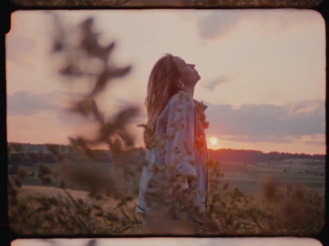 A woman in a meadow looking at the sky at sunset