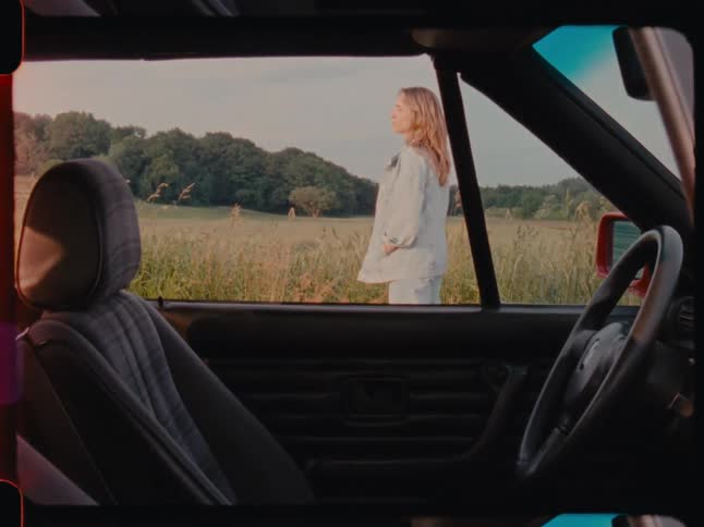 View from inside the vehicle with a woman outside next to a field looking upwards