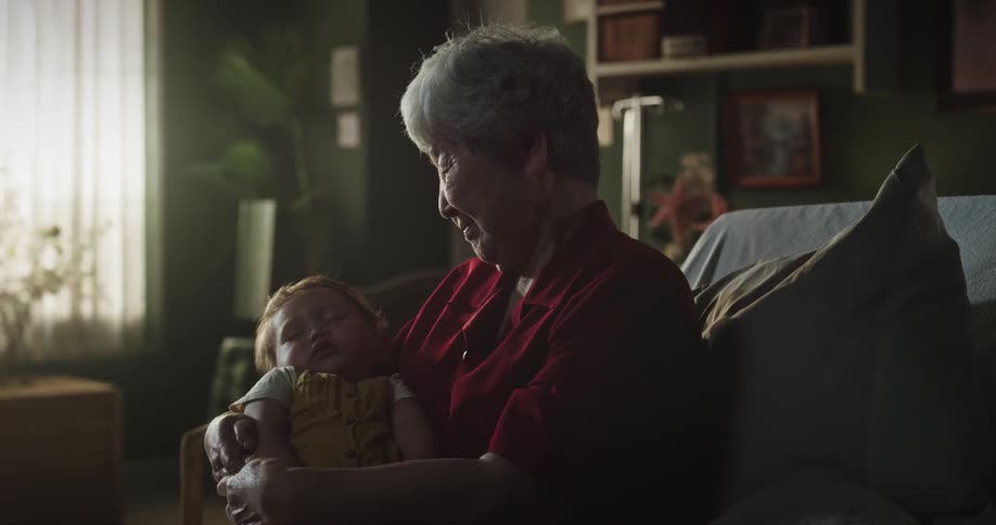An elderly woman holds a baby in her arms and smiles at it