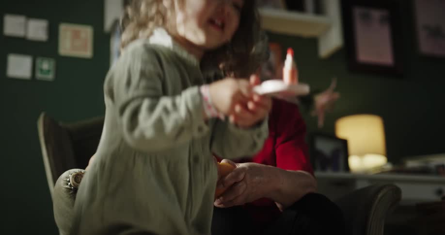 Grandmother peeling an orange next to her daughter while her granddaughter plays with a toy