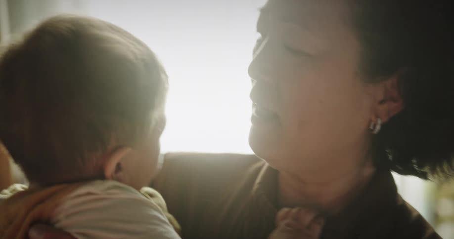Asian woman holds toddler standing in front of window