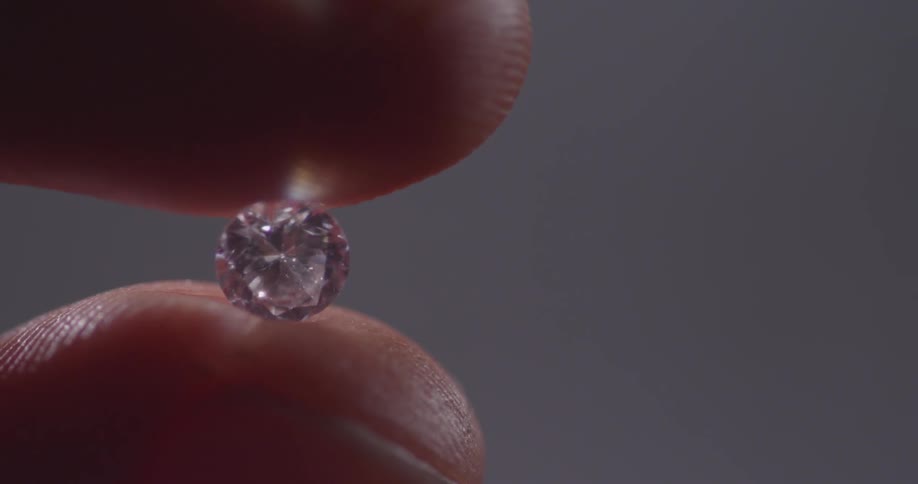 A person twirls a tiny diamond between two fingers