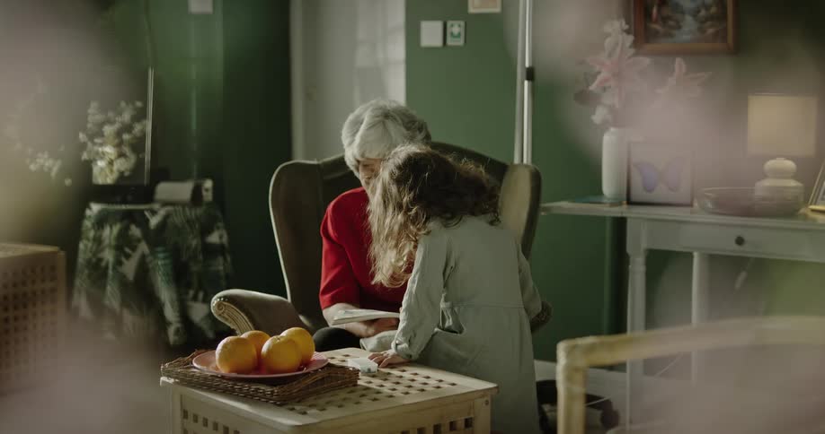 A grandmother reading a story to her granddaughter sitting in an armchair