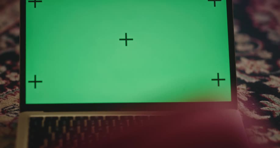 A child types on a laptop computer with a green screen sitting on the floor