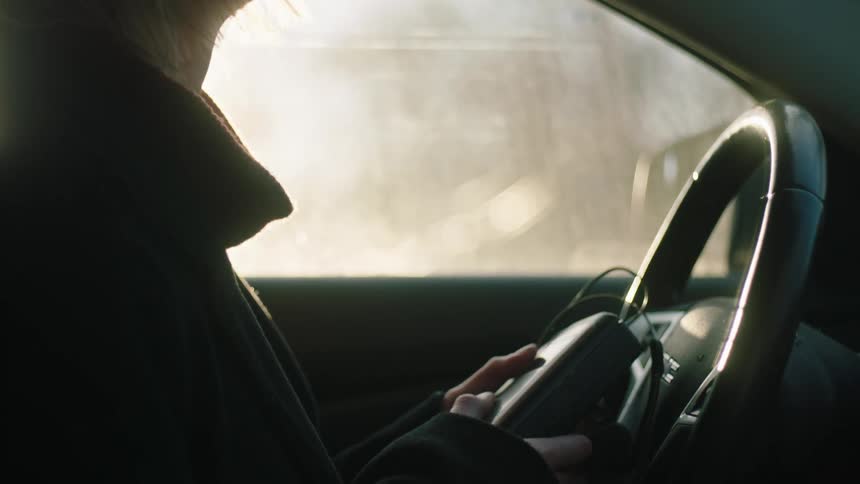 Woman inside the car holding a music device and angrily throwing it to the side