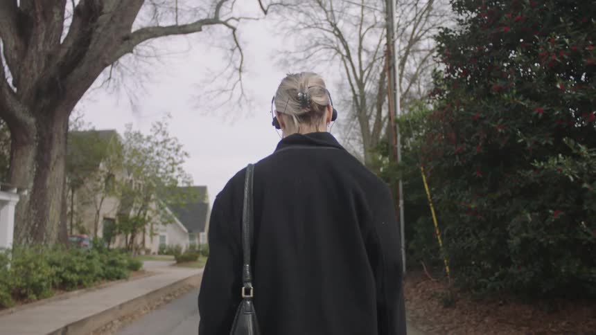 A lady putting on a black coat is walking in the neighborhood