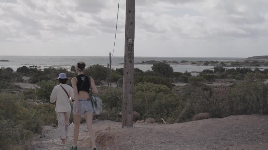 Two females with side bags walking on a sandy path during the day