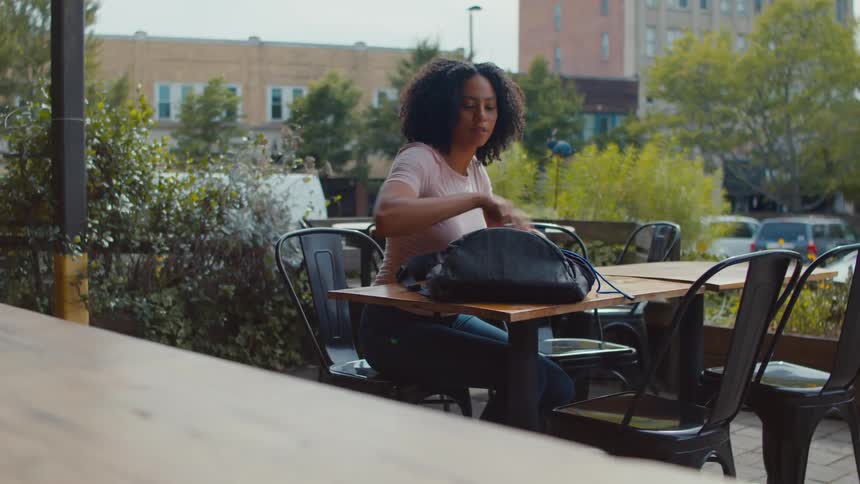 Lady opened a bag while seated at a table outdoor during the day