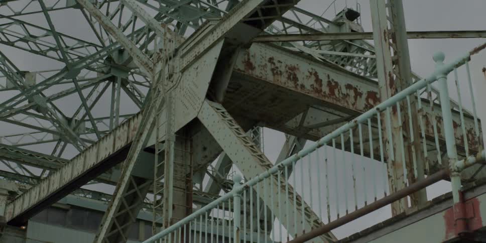 A rusty steel bridge towers above on an overcast day