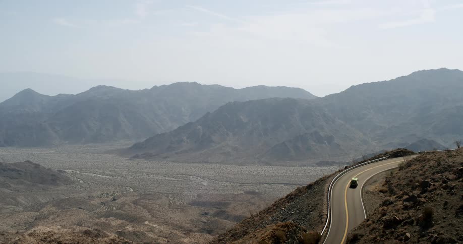 A trucks travel around the curve of a mountain road with mountains in the distance