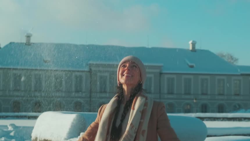 A ladyplaying with snow by throwing it up in the sky