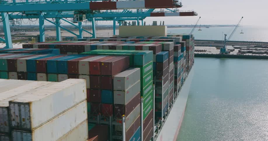 Industrial loading arms stretch over stacked shipping containers at the loading dock