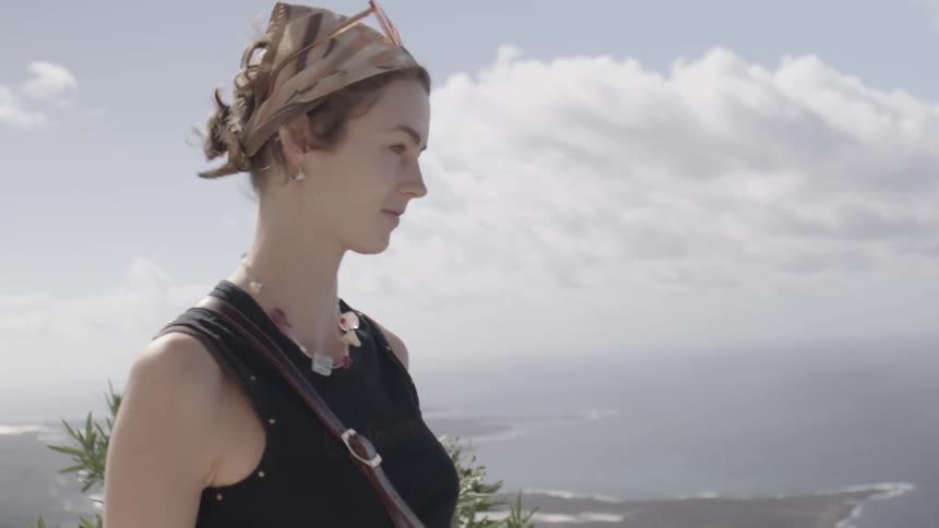 Woman stands on promontory overlooking beach on a cloudy day