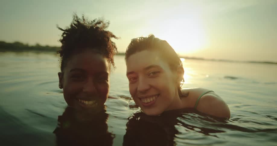 Portrait of two friends by the river smiling with the sun on the horizon