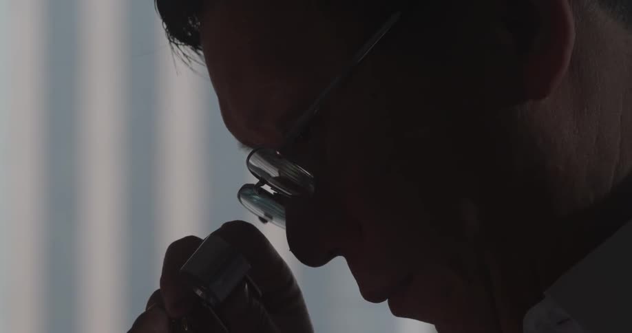 A man inspects a stone with a magnifying glass