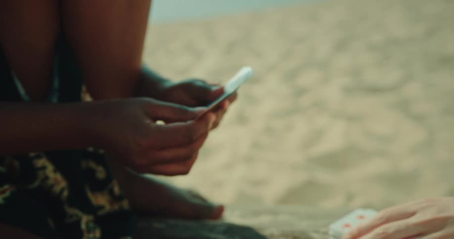 Closeup of two womens hands playing cards on top of a tree trunk on the beach sand