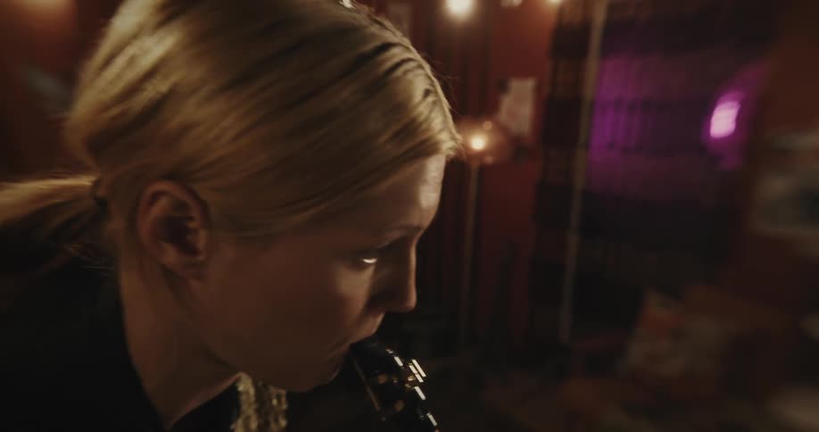 A woman is standing inside a room playing a saxophone