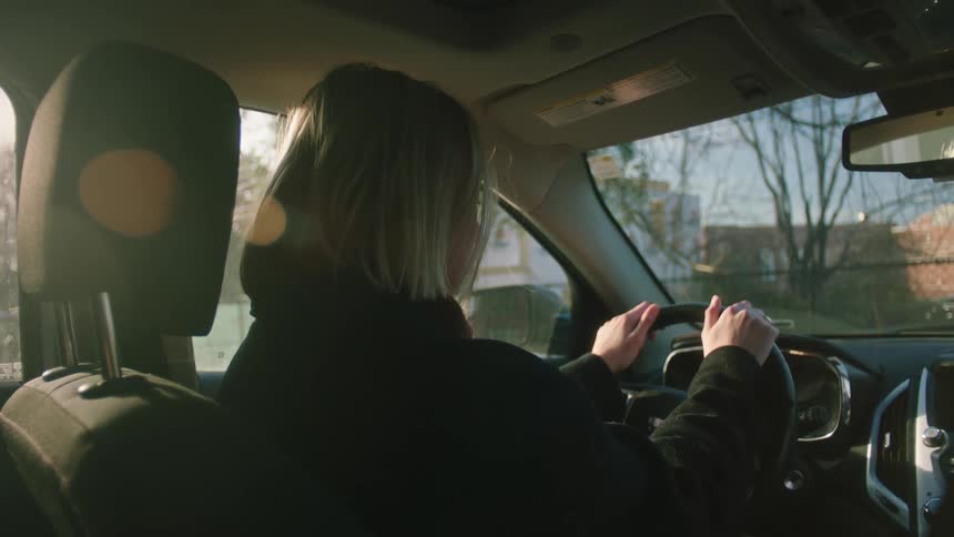 Woman inside a car with hands on the steering wheel and a facial expression of concern