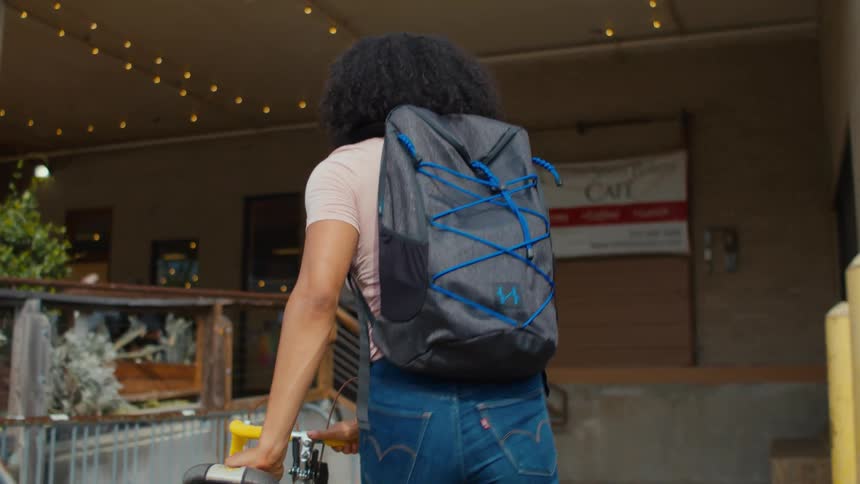 Woman wearing backpack walks bike near plants