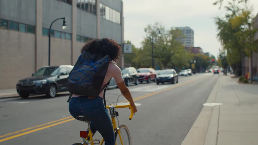 A woman on a bicycle pedaling down a street in an urban neighborhood