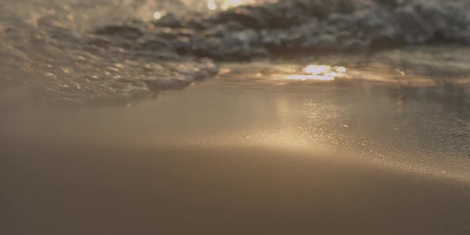 Water splashes up on a sandy beach on a sunny day