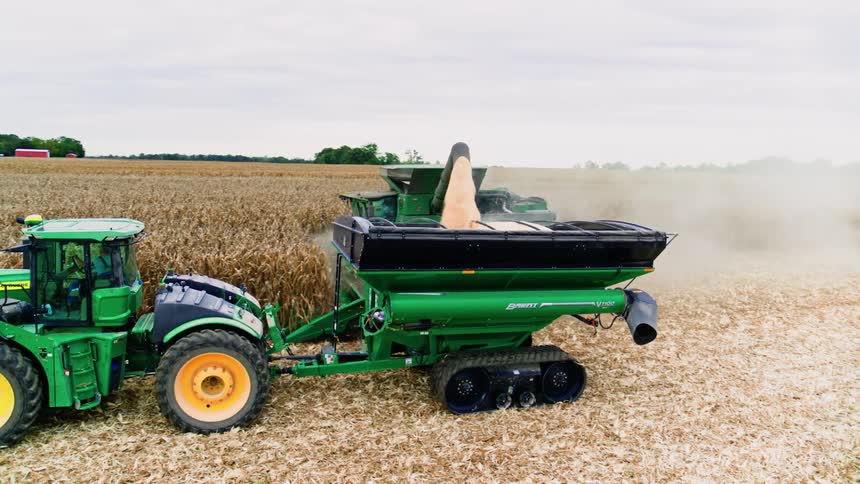 Up close shot of grains spilling into a harvest cart next to a combine collecting the seasons bounty