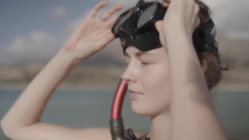 A woman watching the sea and putting on diving goggles