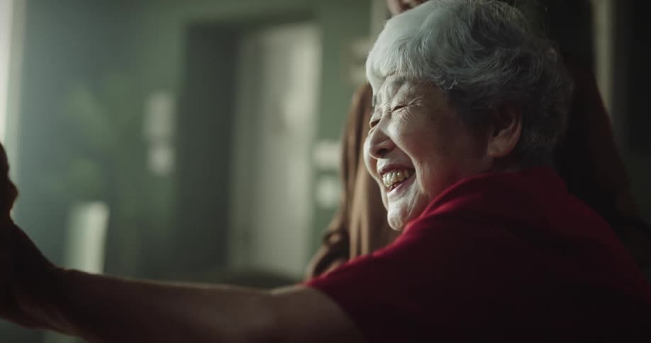 Elderly woman smiling while touching a baby held by another person in a room