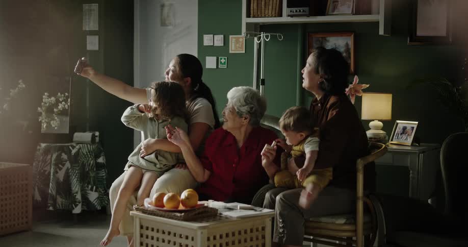 A family is sitting on a sofa and a woman takes a selfie of everyone