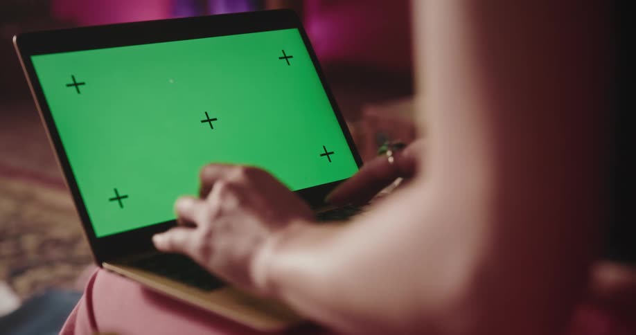 A woman is typing on a laptop computer with a green screen