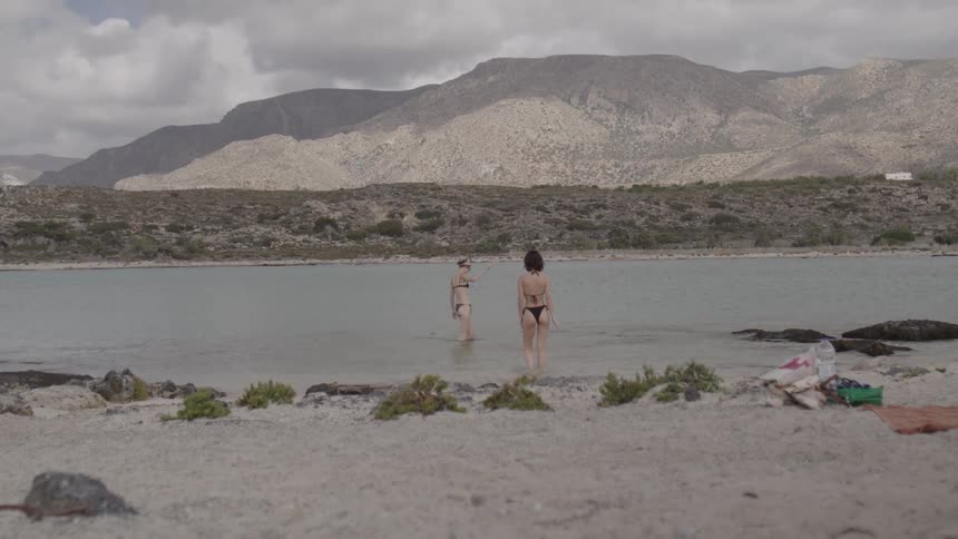 Two female friends in a bikini are walking in the water
