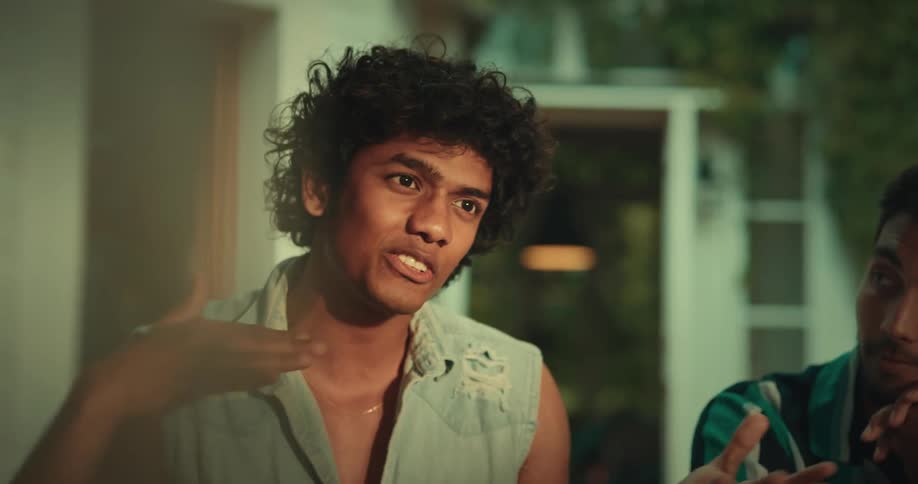 One man smiles and nods while watching his friend talk to others