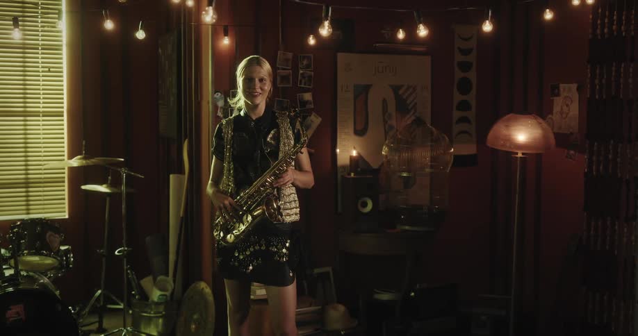 A woman walks out of the room holding a saxophone