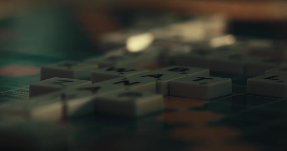 Someone playing scrabble putting pieces on the board to form words