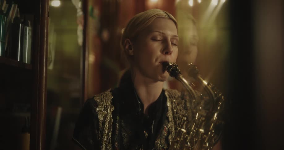 A woman is standing inside a room playing a saxophone