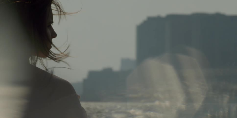 A woman stands on the shoreline as the wind blows her hair